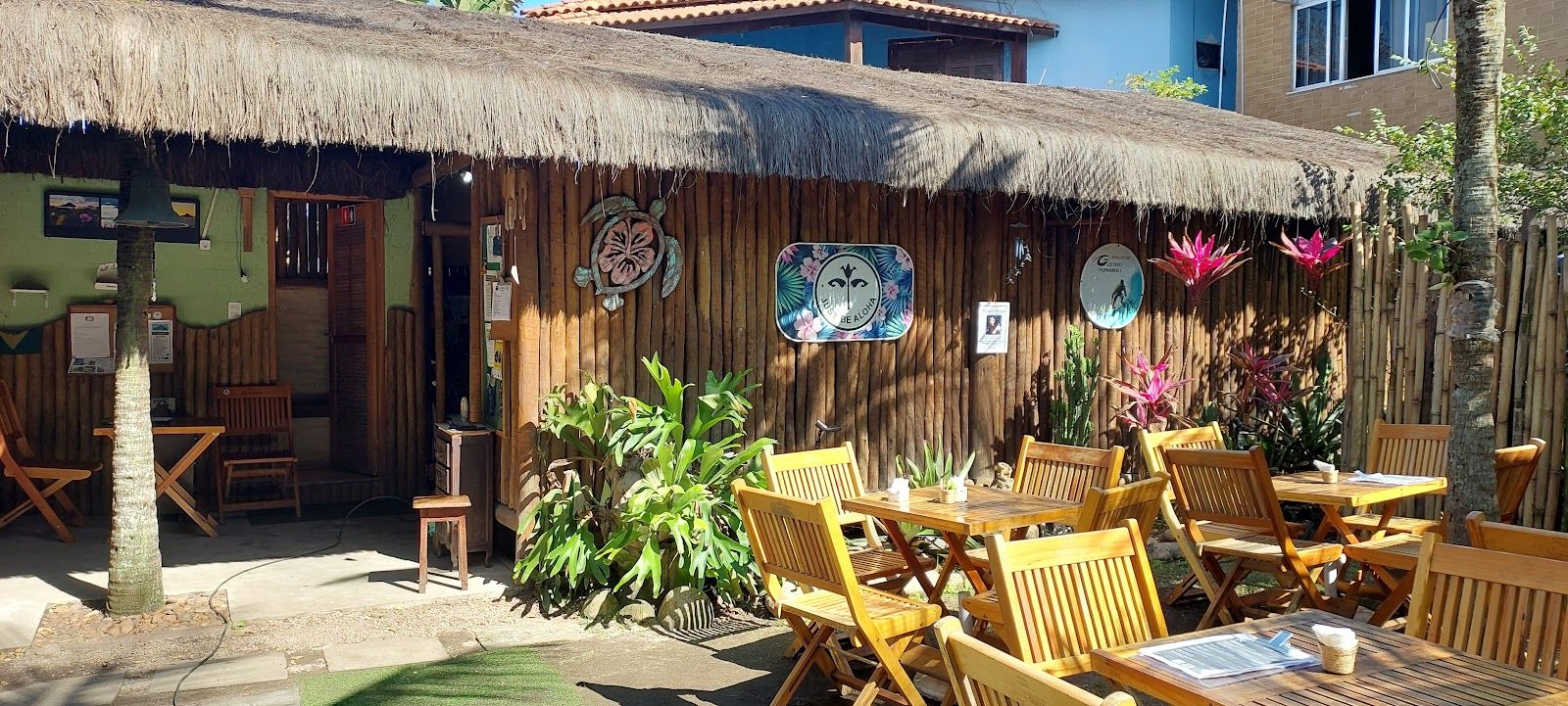 Fachada do Vibes com cobertura de sapé e mesas de madeira do lado de fora